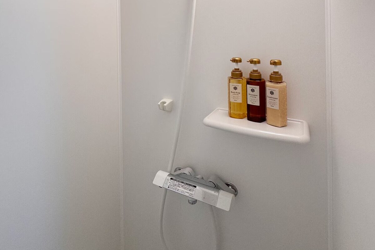 A shower with a handheld showerhead, a wall-mounted light, and a shelf with toiletries.