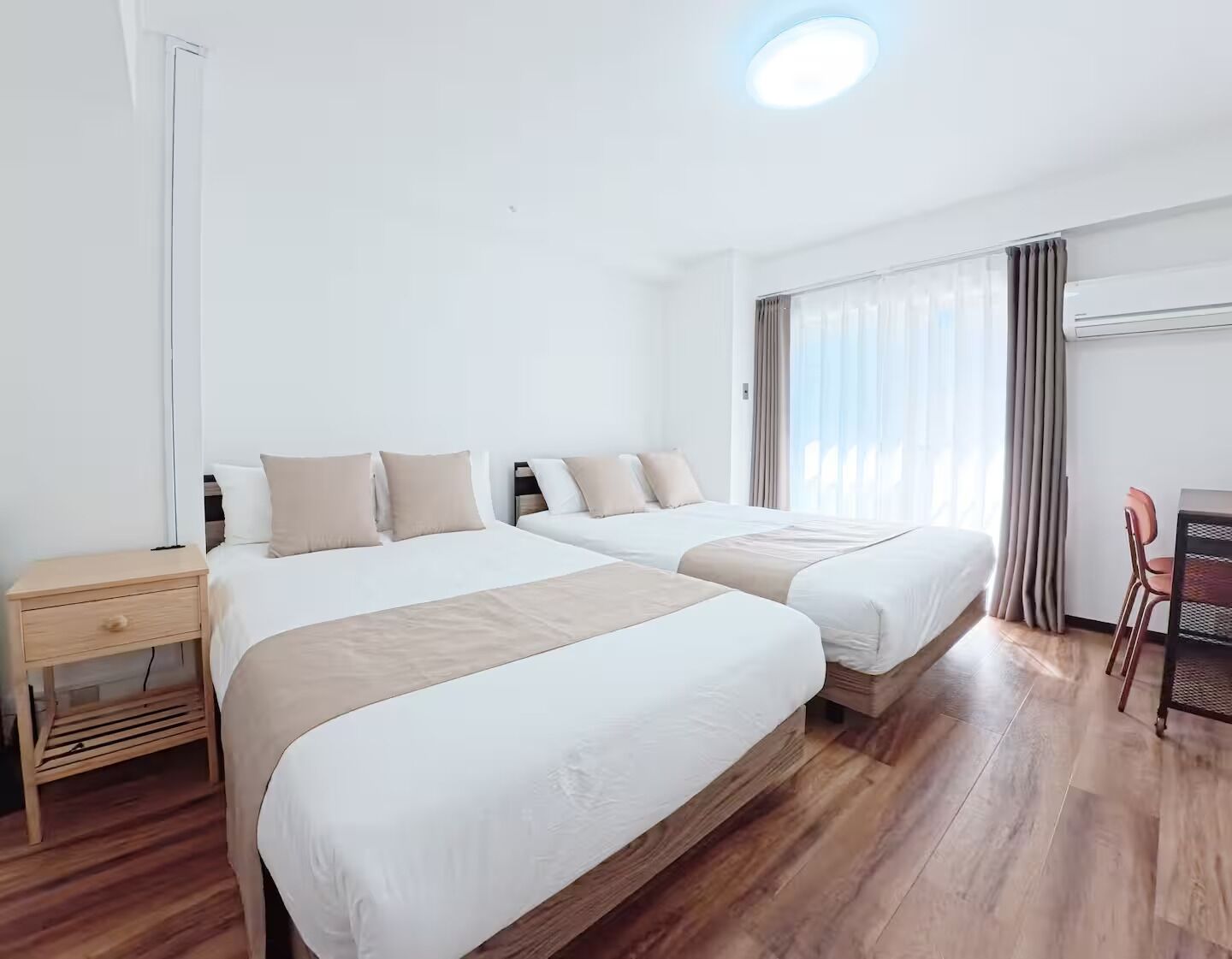 A hotel room with two beds, a desk, a chair, and a window with curtains.