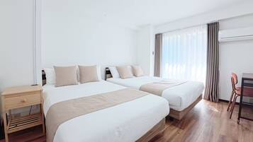 A hotel room with two beds, a desk, a chair, and a window with curtains.
