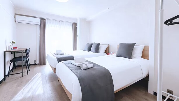 Habitación de hotel con dos camas, un escritorio, sillas y una ventana con cortinas.