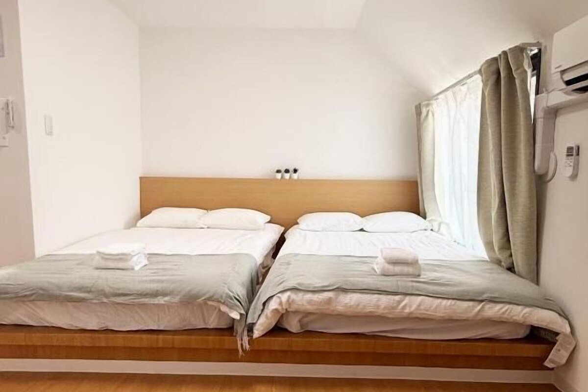 A double bed with a wooden headboard, a bedside table, and a curtain on the right side.