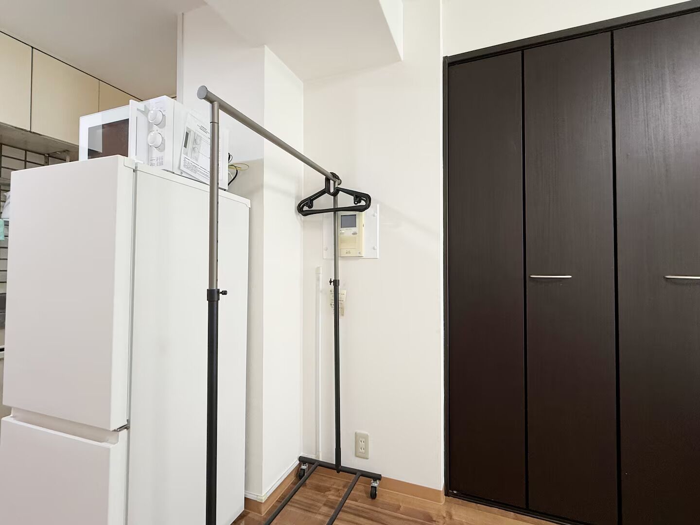 A kitchen with a white refrigerator, a microwave, and a hanging rack. There is a dark wooden door and a white wall.