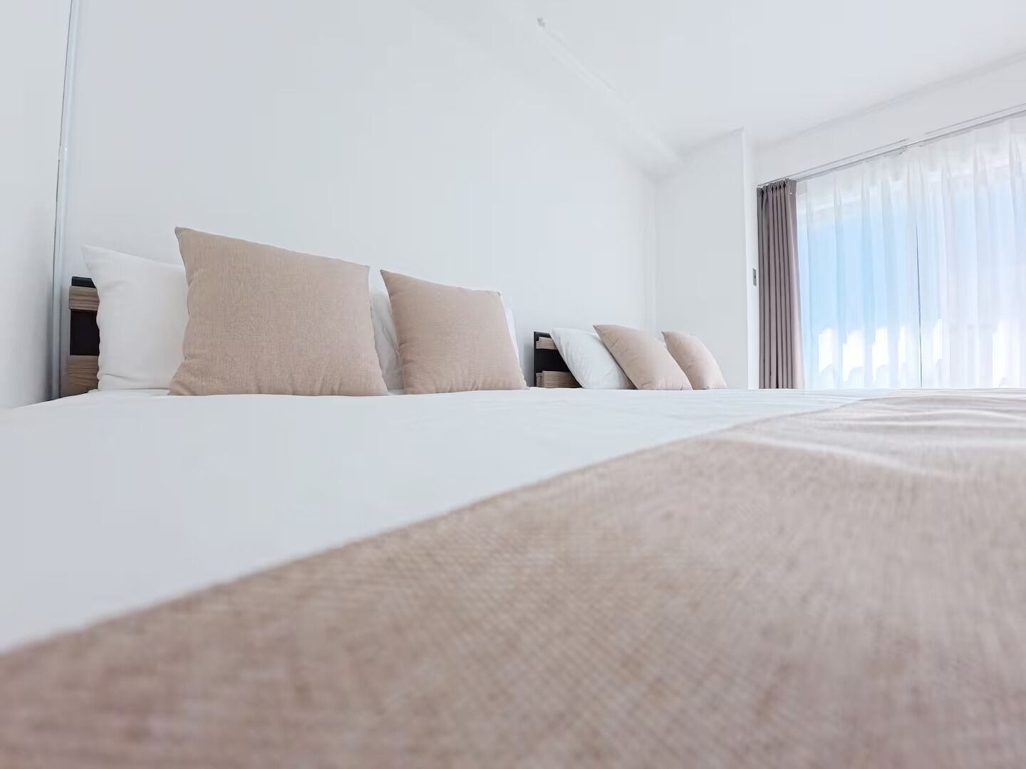 A hotel room with a large bed, multiple pillows, a bedside table, and a window with curtains.