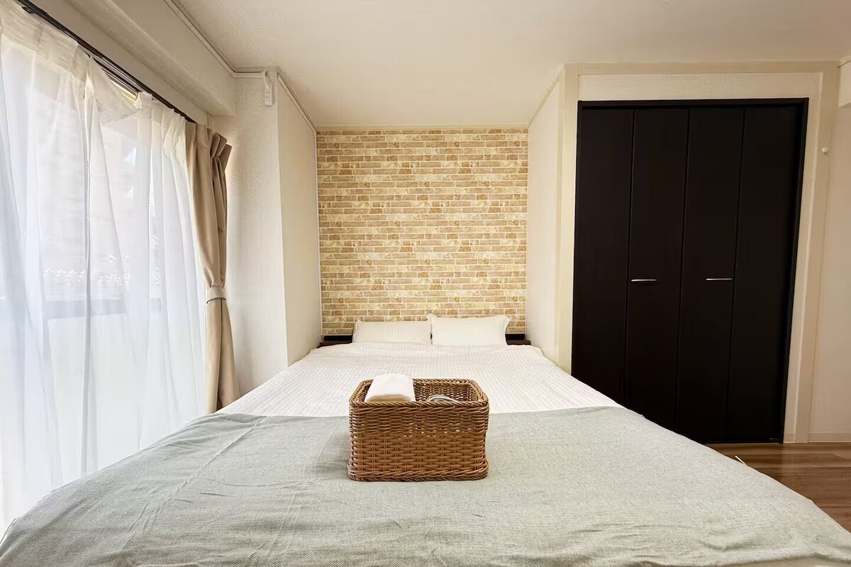 A hotel room with a bed, a brick wall, a dark door, and a wicker basket on the bed.