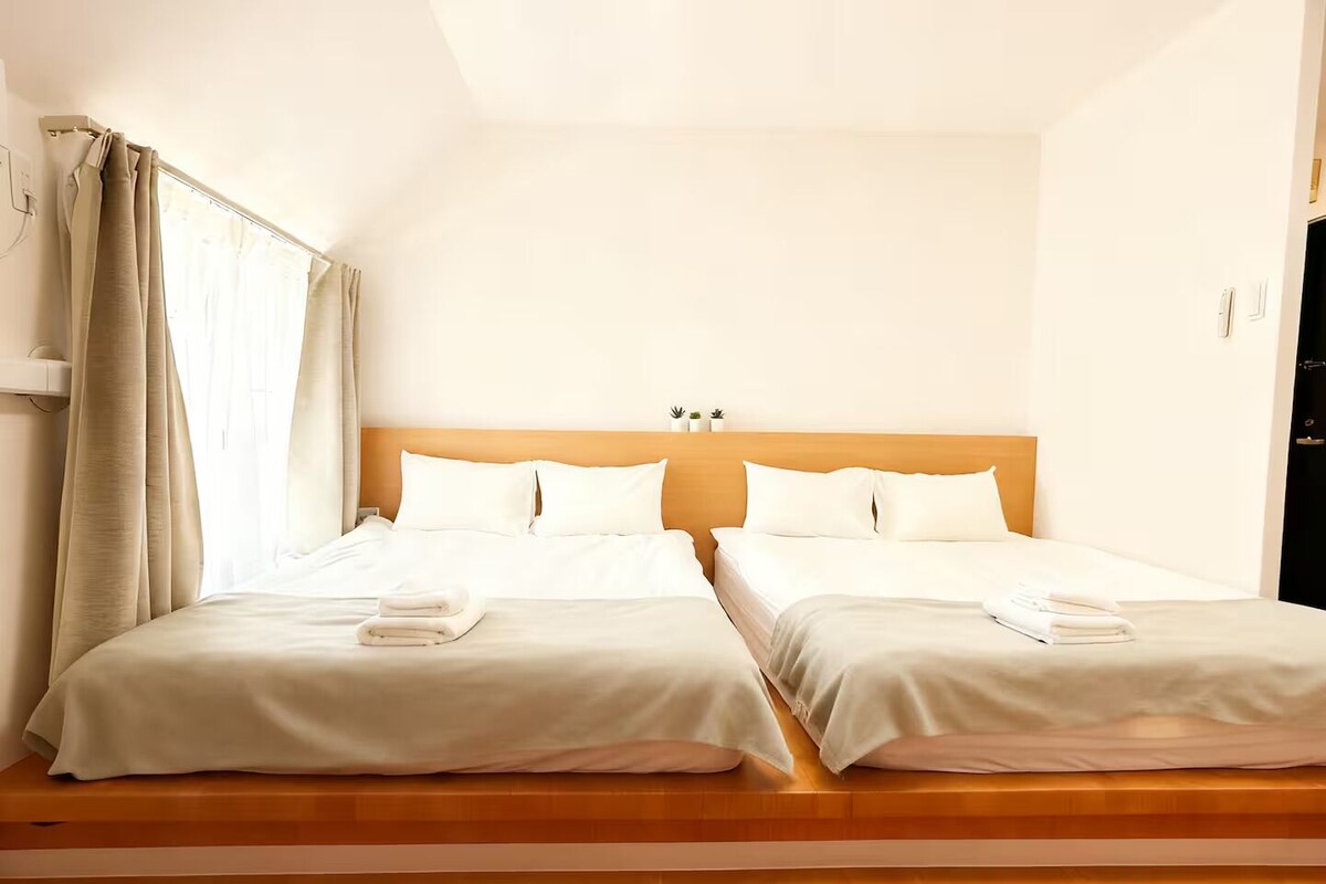 A hotel room with two beds, a wooden headboard, a window with curtains, and a small plant on the nightstand.