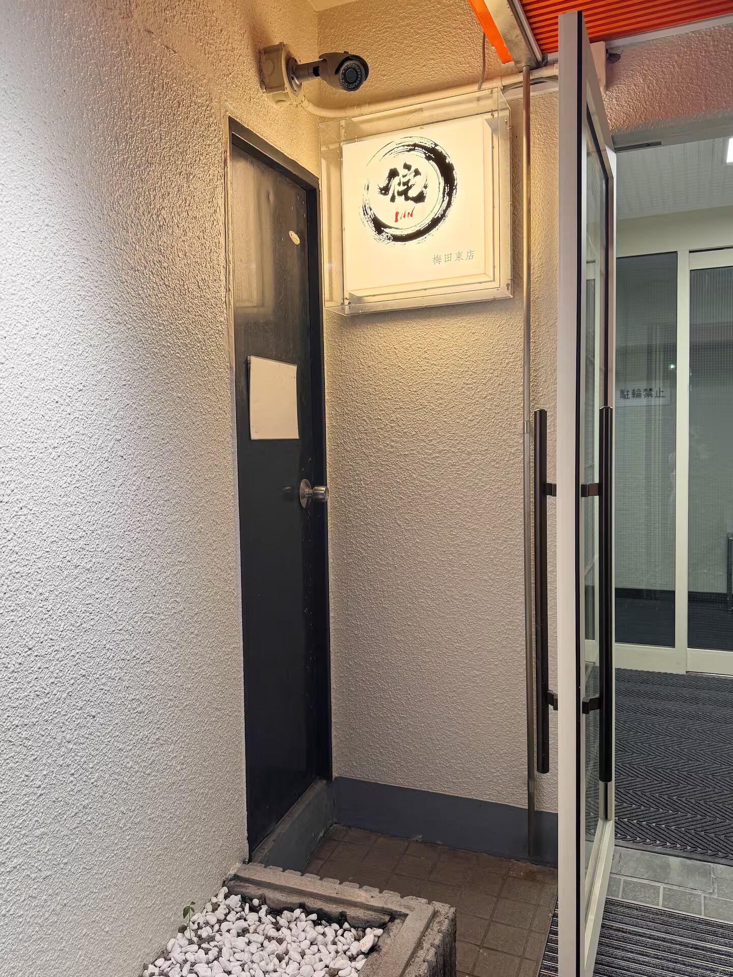 A door with a sign, a security camera, and a small garden area with white pebbles.