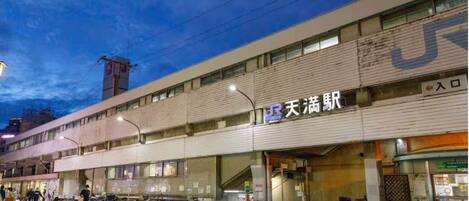Un edificio de varios pisos con un gran letrero que dice '天満橋' y una zona de estacionamiento para bicicletas enfrente.