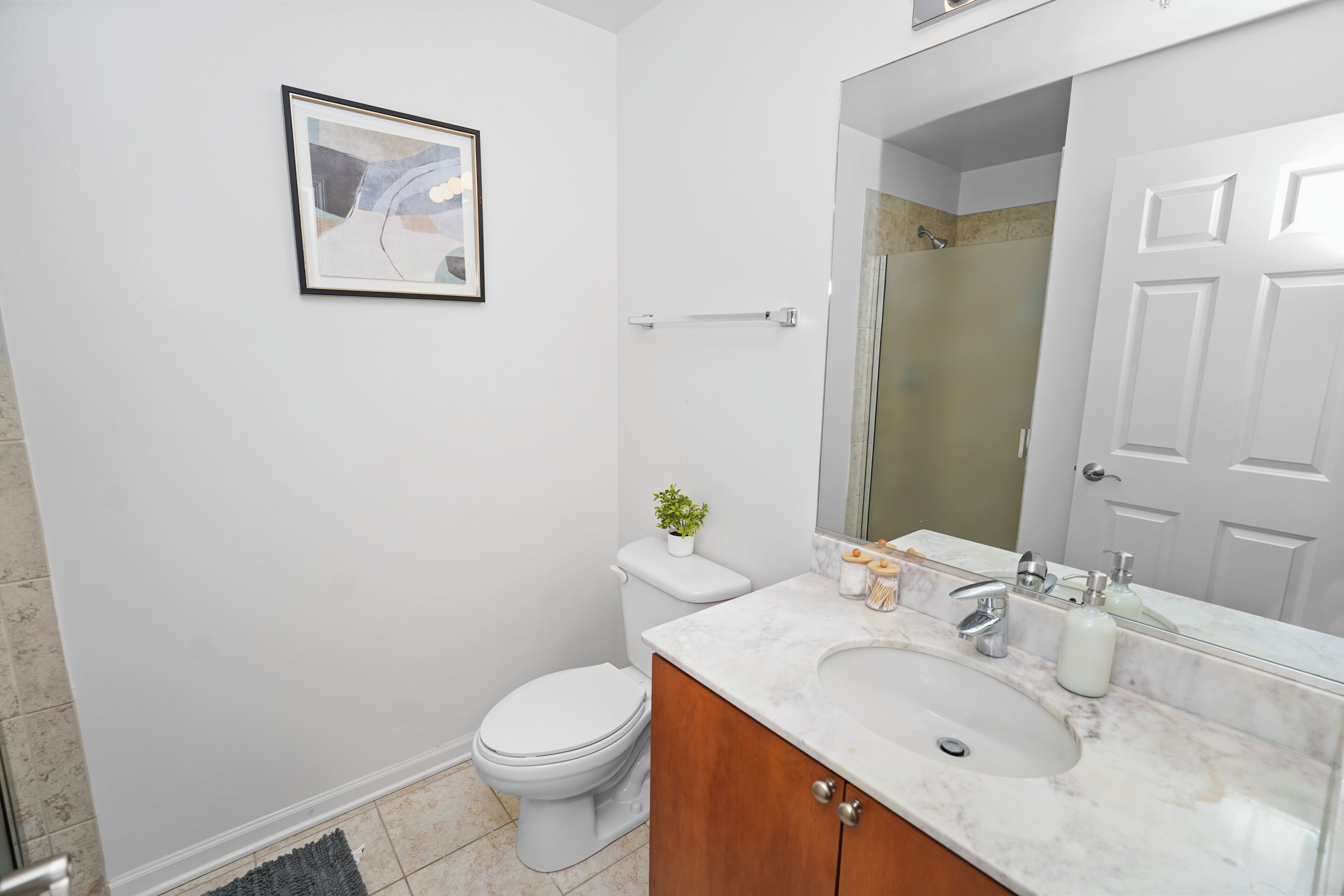 A bathroom with a toilet, sink, mirror, and framed picture on the wall.