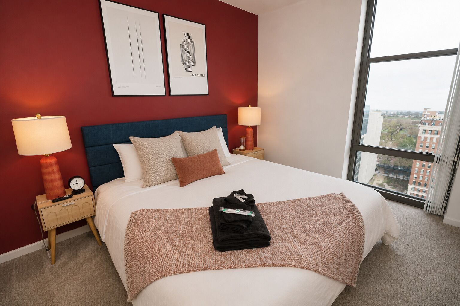 A hotel room with a large bed, two bedside tables with lamps, a red accent wall, and two framed pictures.