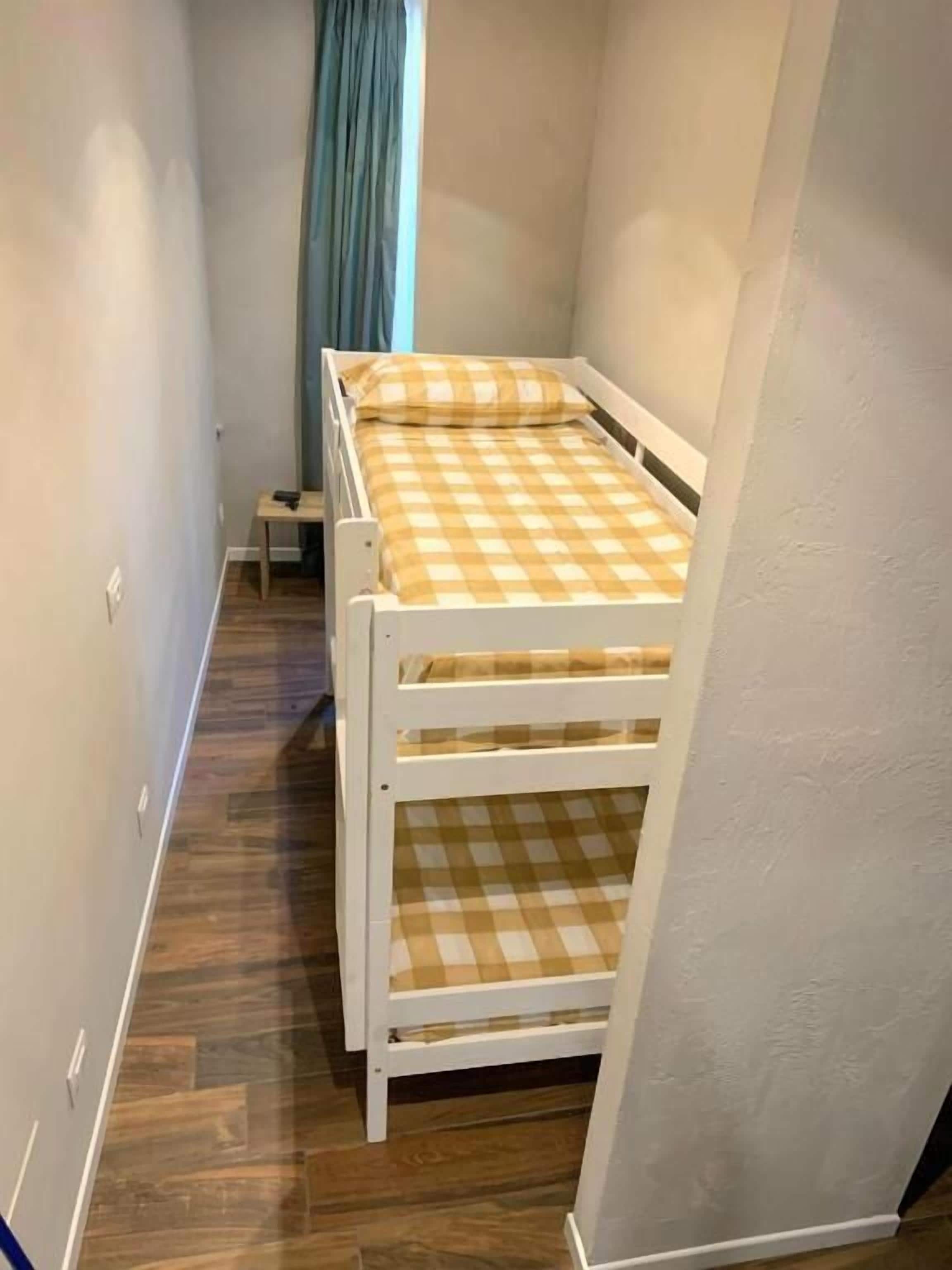 Una habitación pequeña con una cama individual, piso de madera y una ventana con cortinas.