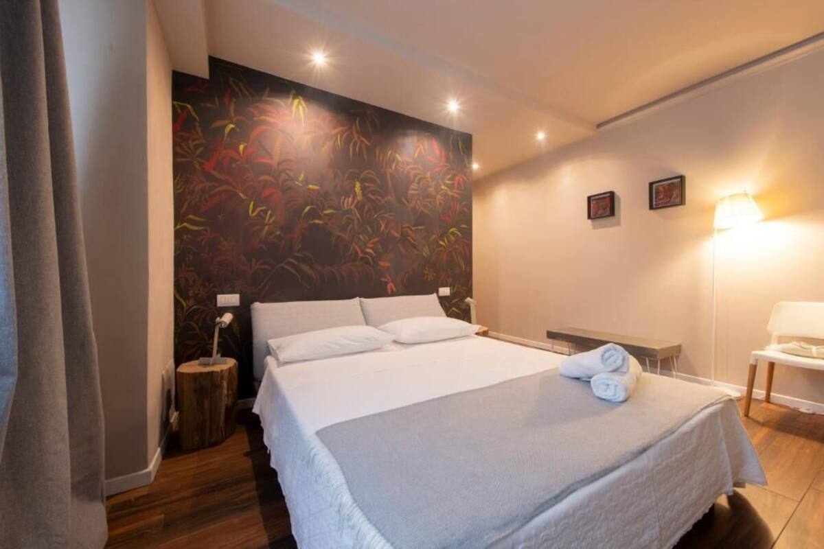 A hotel room with a large bed, a bedside table, a lamp, and a wall with a floral mural.