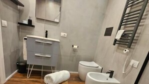 Un baño moderno con tocador, inodoro, bidé y un taburete de madera con una toalla.