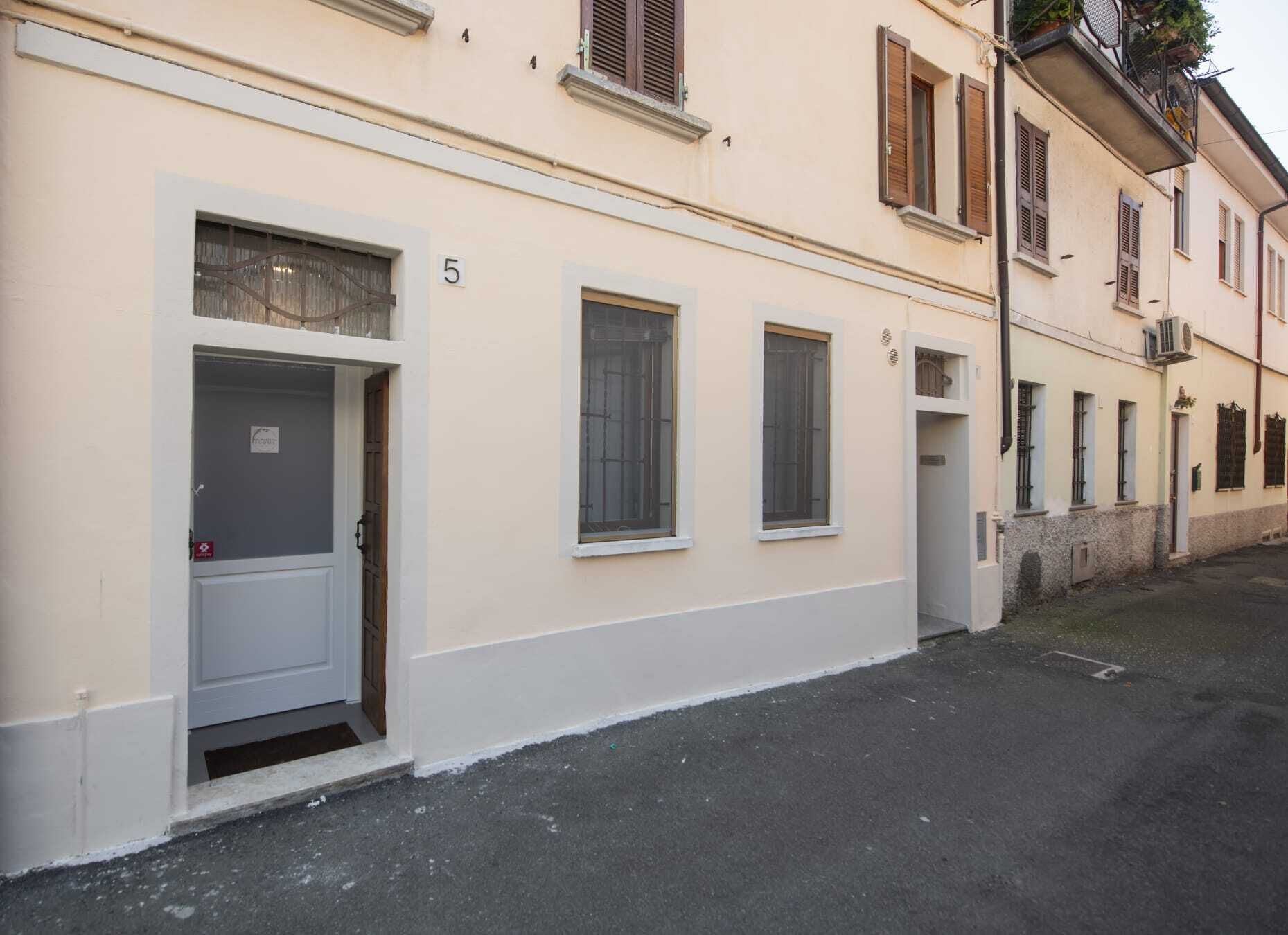 Un edificio con facciata bianca, numero 5, con una porta che include una finestra, un piccolo balcone e un ingresso stretto.