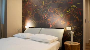 A bedroom with a bed, white bedding, a nightstand, a wall-mounted lamp, and a wooden tree stump.