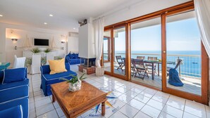 Un salon avec un canapé, une table basse et un téléviseur. Il y a un balcon avec une table et des chaises.
