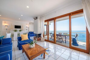 Ein Wohnzimmer mit einer Couch, einem Couchtisch und einem Fernseher. Es gibt einen Balkon mit Tisch und Stühlen.