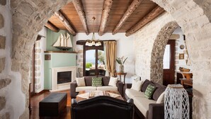 A rustic room with stone walls, wooden beams, a fireplace, and a sofa set. - Your Villa (Chania)