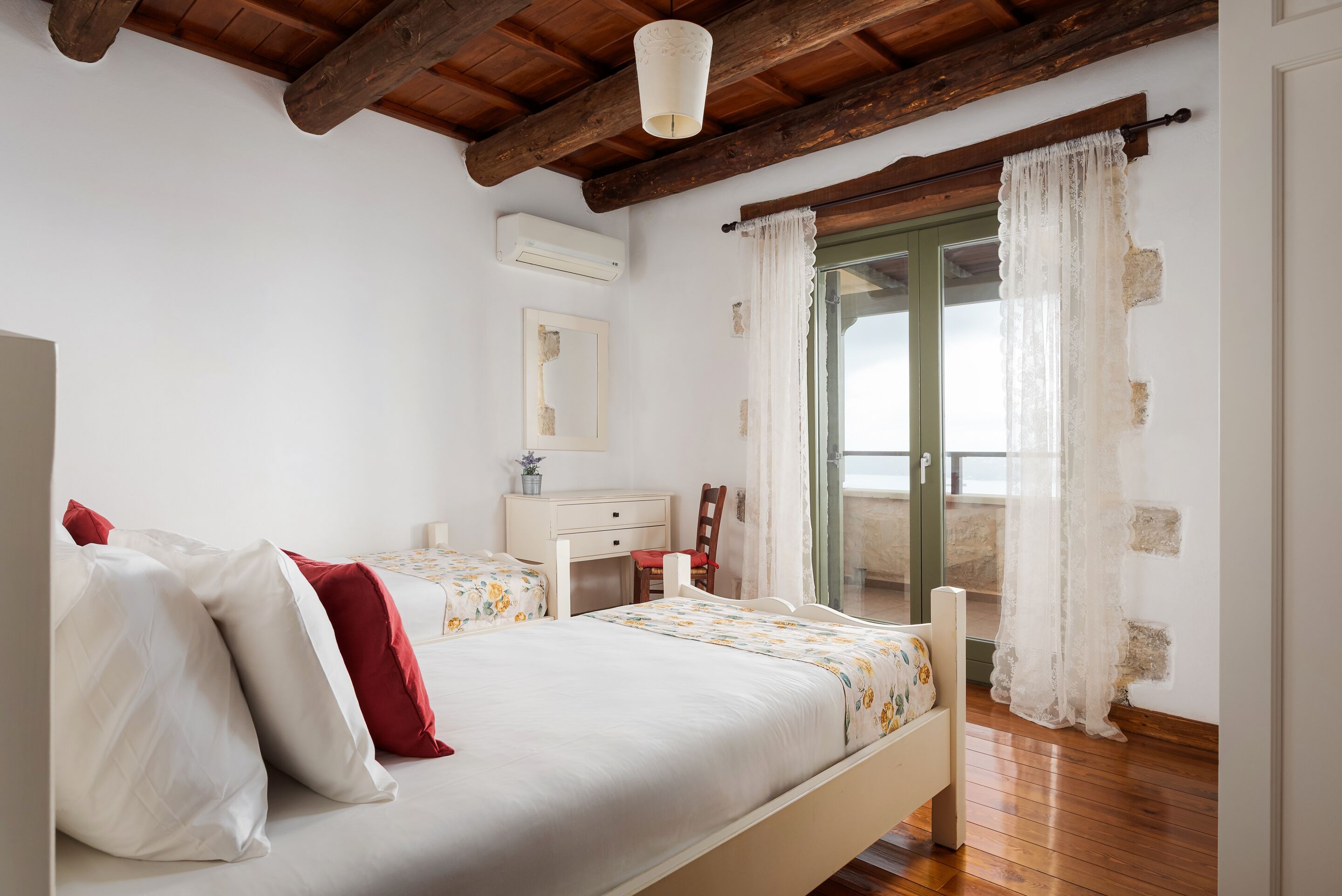 Un dormitorio con techo de madera, cama con ropa de cama blanca y roja, un escritorio y una ventana con cortinas.