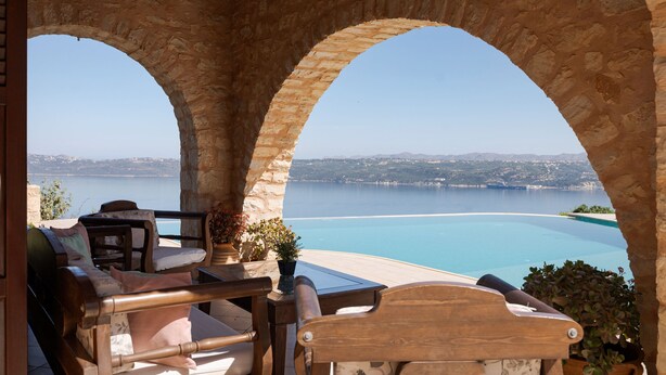 A stone archway leading to a terrace with a view of a large body of water and distant hills. - Your Villa (Chania)
