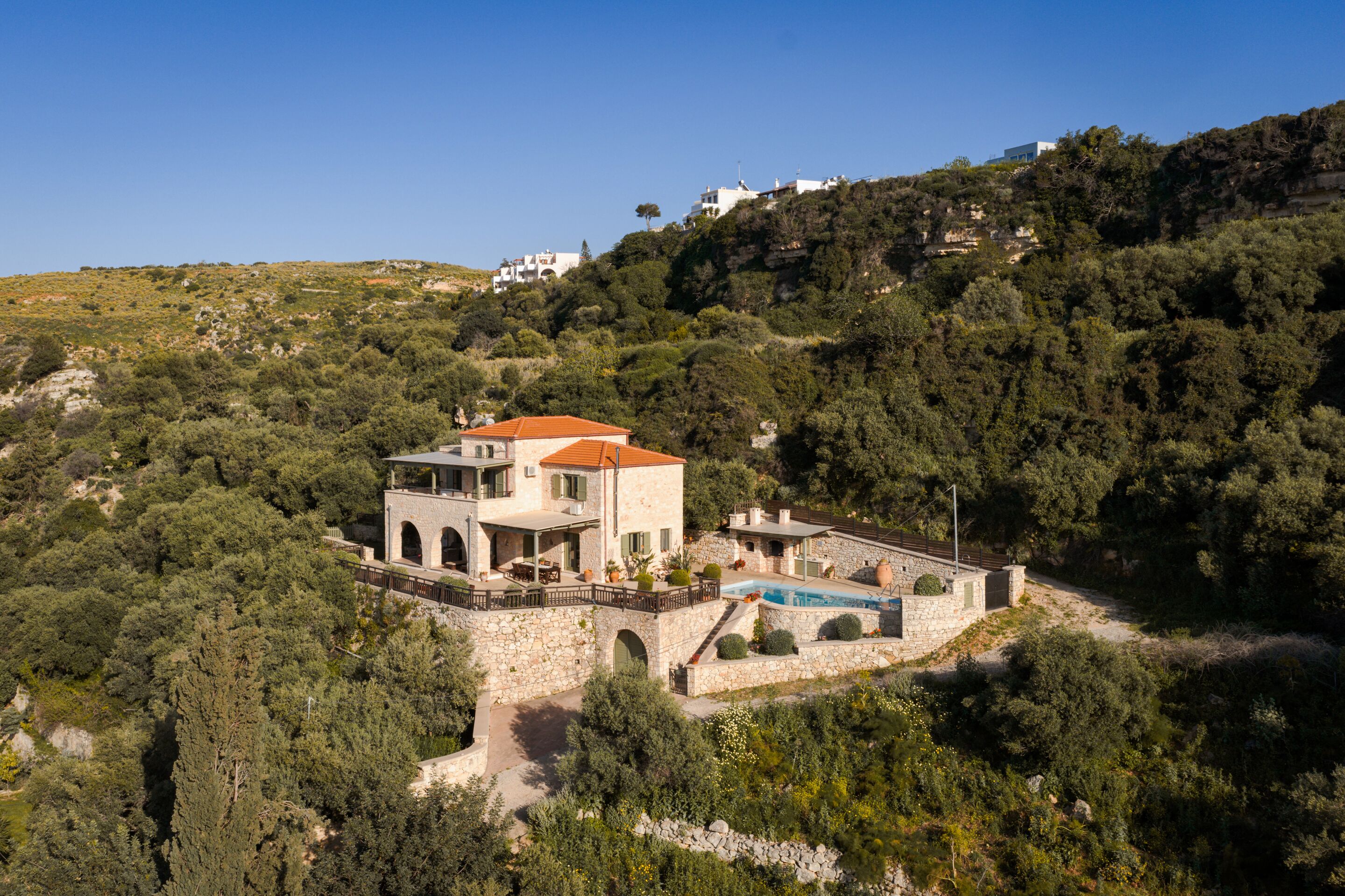 Una villa de piedra con piscina, rodeada de vegetación densa y colinas.