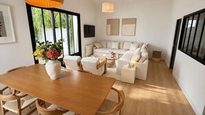 Una sala de estar moderna con una mesa de comedor de madera, sofás blancos y un amplio ventanal.