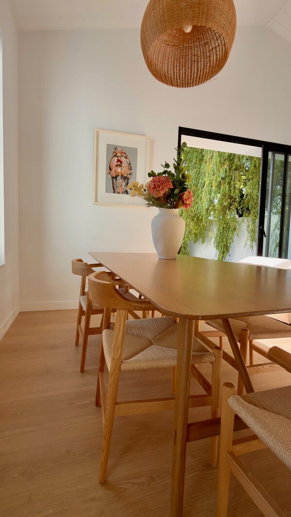 A dining area with a wooden table, chairs, a woven pendant light, a vase with flowers, and a framed artwork on the wall. - Maison Vicoli, entièrement neuve & rénovée, Les Portes en Re, Île de Ré ! (Les Portes-en-Ré)