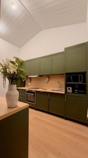 Une cuisine moderne avec des meubles de couleur verte, un plan de travail en bois et un vase rempli de fleurs.