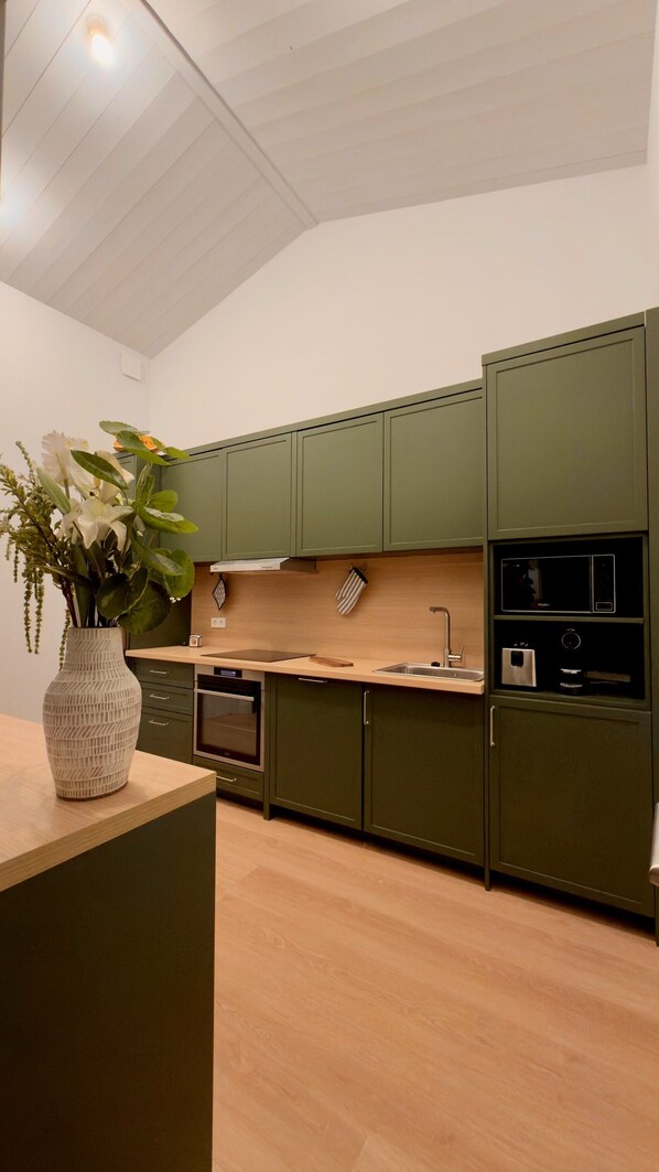 A modern kitchen with green cabinets, a wooden countertop, and a vase with flowers. - Maison Vicoli, completely new & renovated, Les Portes en Ré, Île de Ré! (Les Portes-en-Ré)