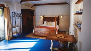Una stanza con un letto a baldacchino in legno, un tavolino con sedie, un lampadario e uno scaffale con soprammobili.