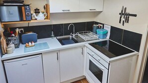 Una cucina compatta con un velux, pensili bianchi, un piano di lavoro nero e una lavastoviglie piccola.
