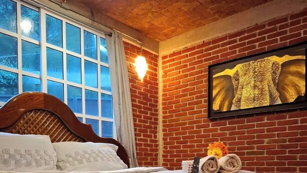 A bedroom with a large bed, a brick wall, a window, and a framed picture.