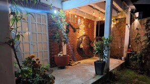 A covered outdoor area with a brick wall, potted plants, and a hanging chair.