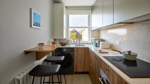A compact kitchen with a window, a sink, a stove, and a small dining area with stools.