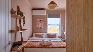 A bedroom with a bed, a shelf with items, a window, and a view.