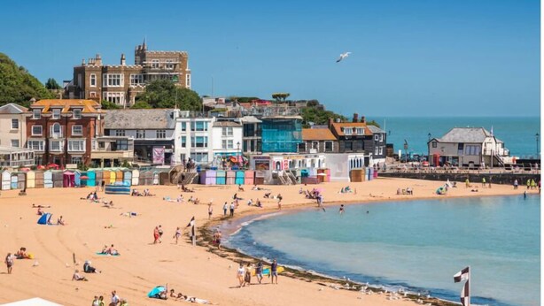 A beach with buildings in the background, including a large castle-like structure.