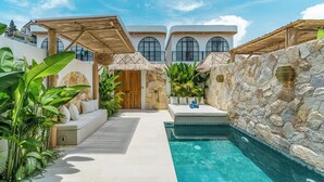 A pool area with a stone wall, a wooden pergola, and a white building with arched windows. - Tropical Mediterranean Villas in Canggu (Canggu)