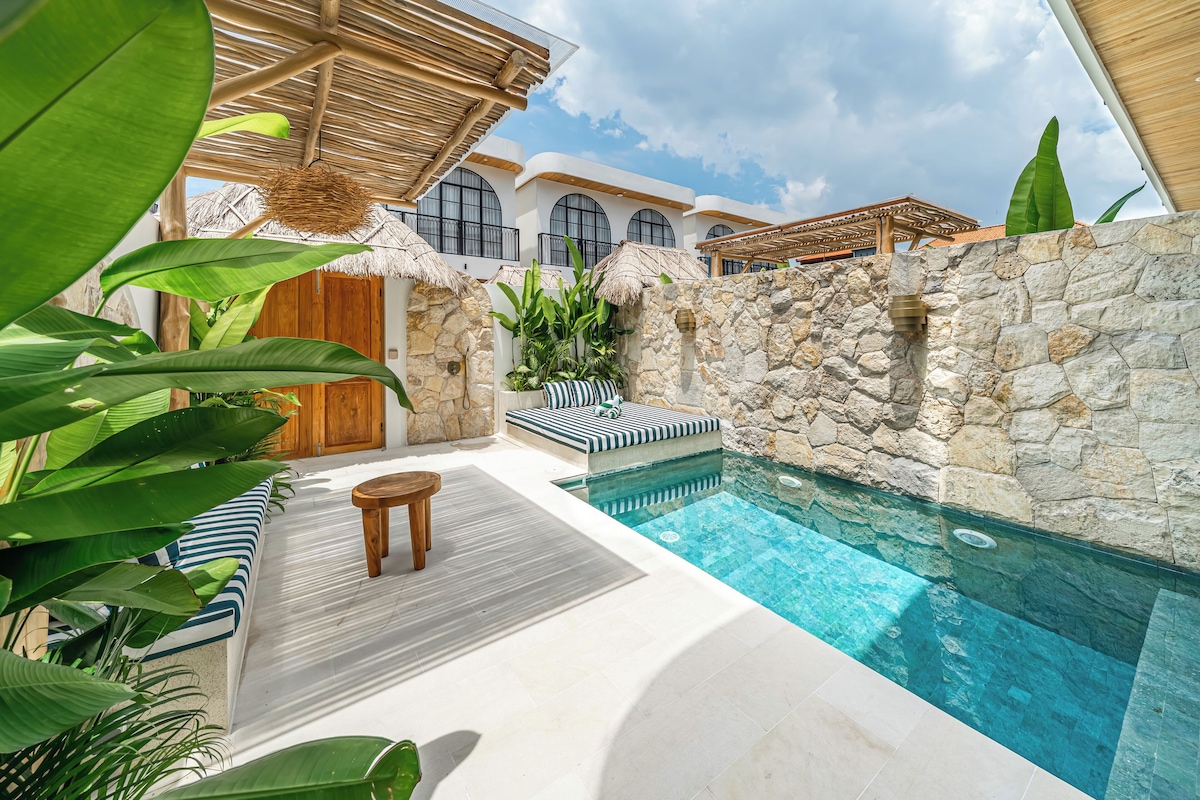 Zona de piscina con muro de piedra, cubierta de madera y estructura de techo de paja.
