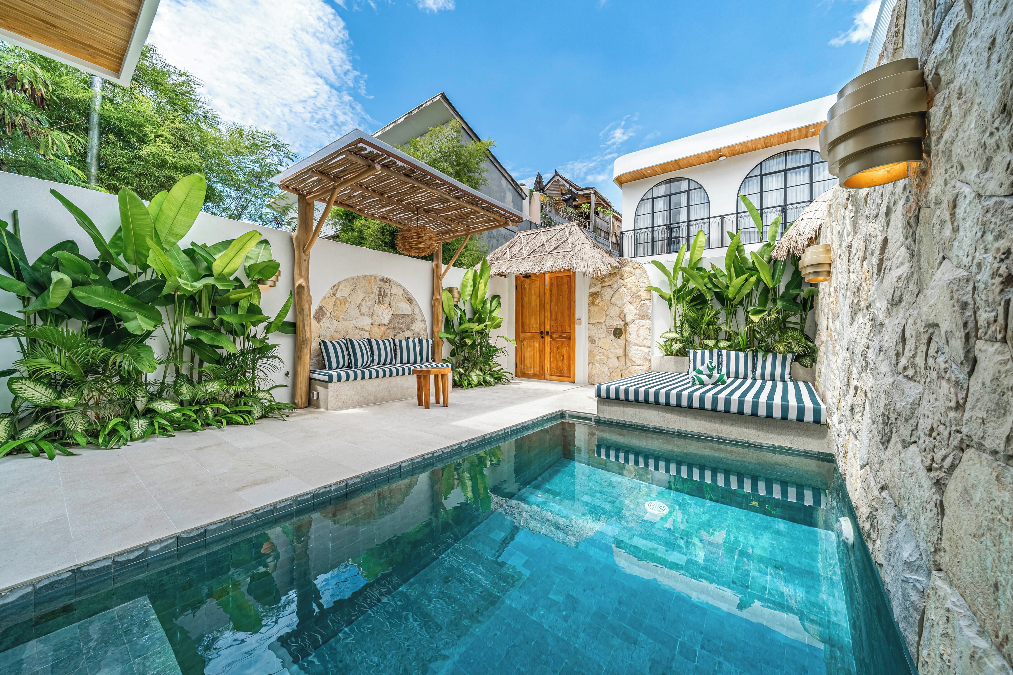 A swimming pool with lounge chairs, a stone wall, and a wooden pergola.