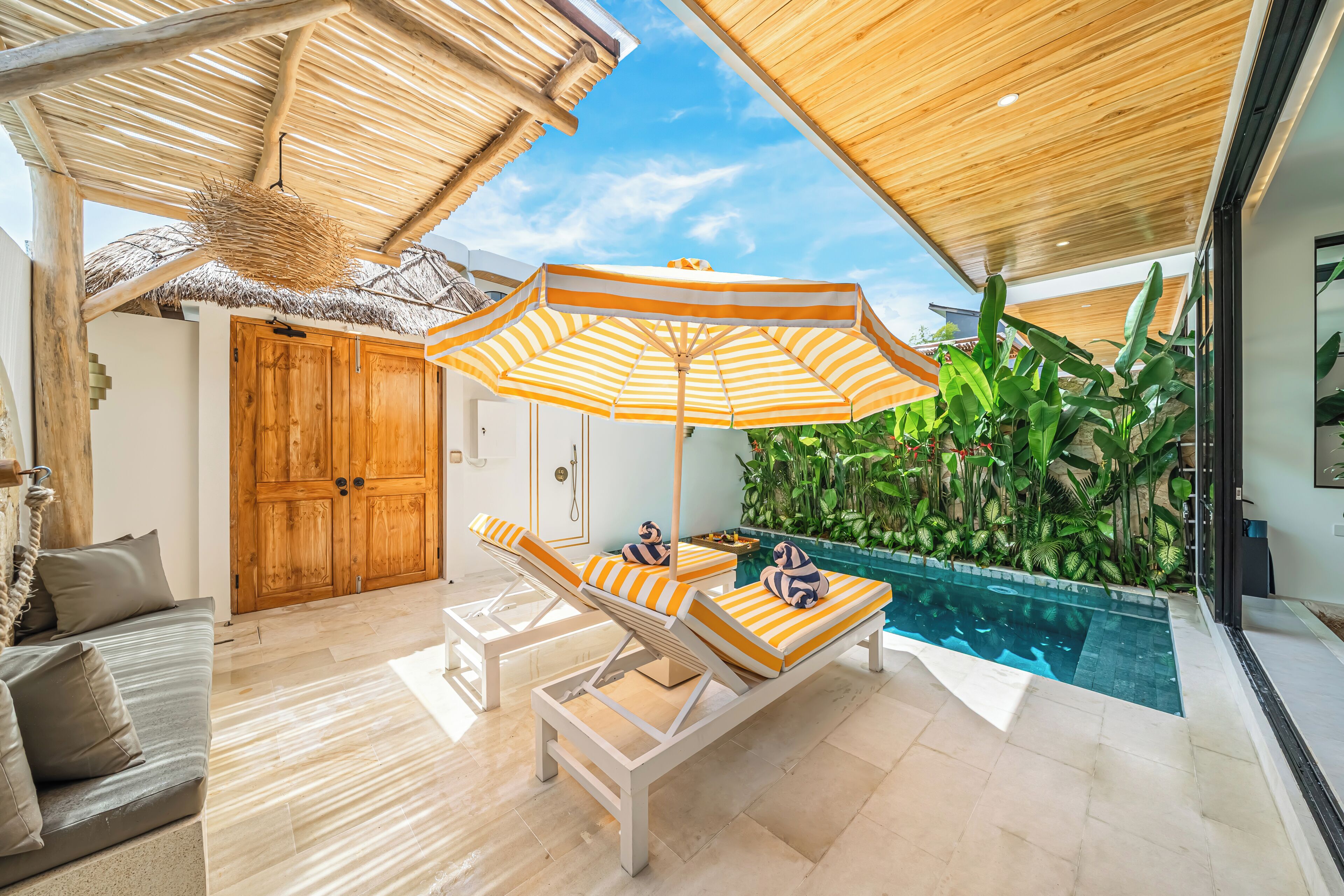 A poolside area with lounge chairs, a wooden door, and a thatched roof.