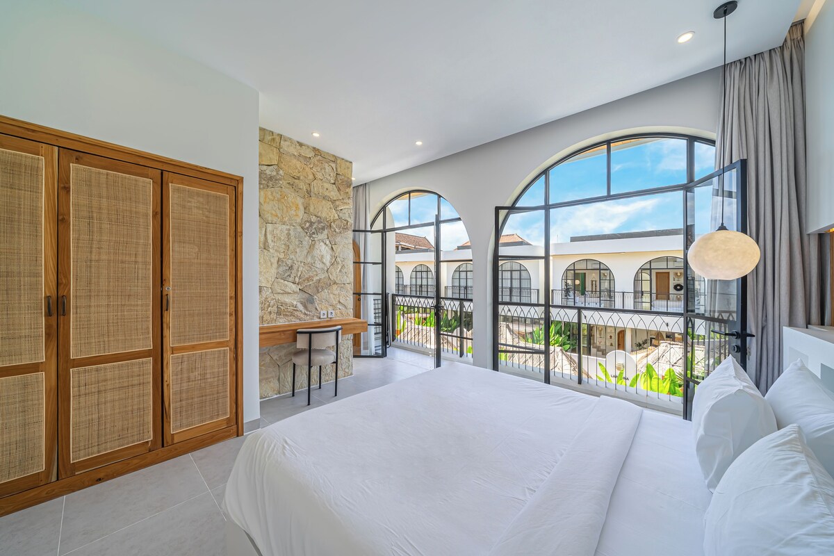 Una habitación de hotel moderna con una cama grande, un armario de madera, una pared decorativa de piedra y un balcón con vistas al patio.