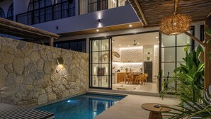 A modern pool area with a stone wall, a dining area with a kitchen, and a hanging light fixture. - Tropical Mediterranean Villas in Canggu (Canggu)