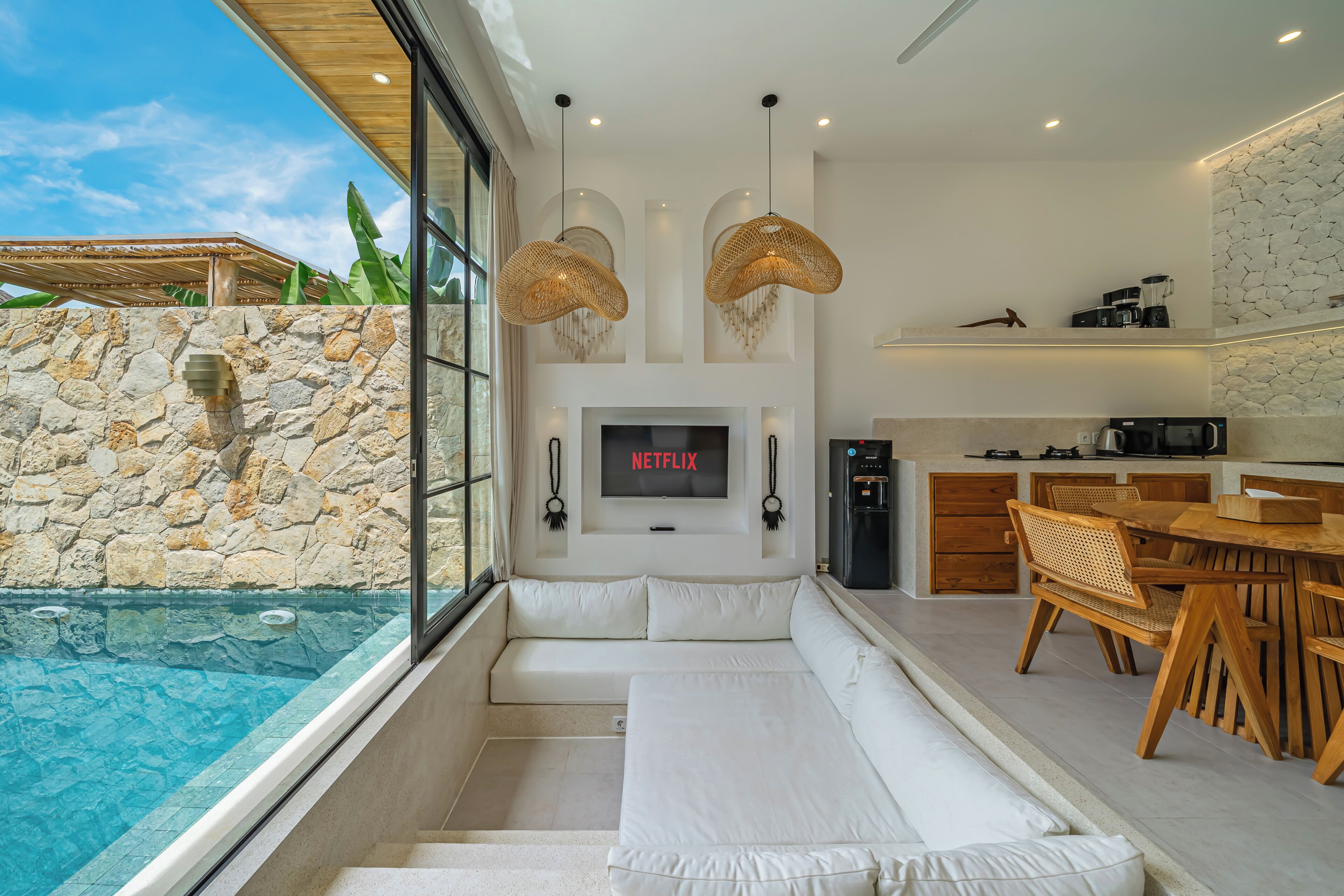 A modern living room with a stone wall, a TV, a pool, and a dining area.