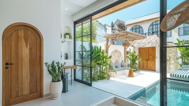 A modern interior with a large glass door, a wooden door, a pool, and a seating area with plants. - Tropical Mediterranean Villas in Canggu (Canggu)