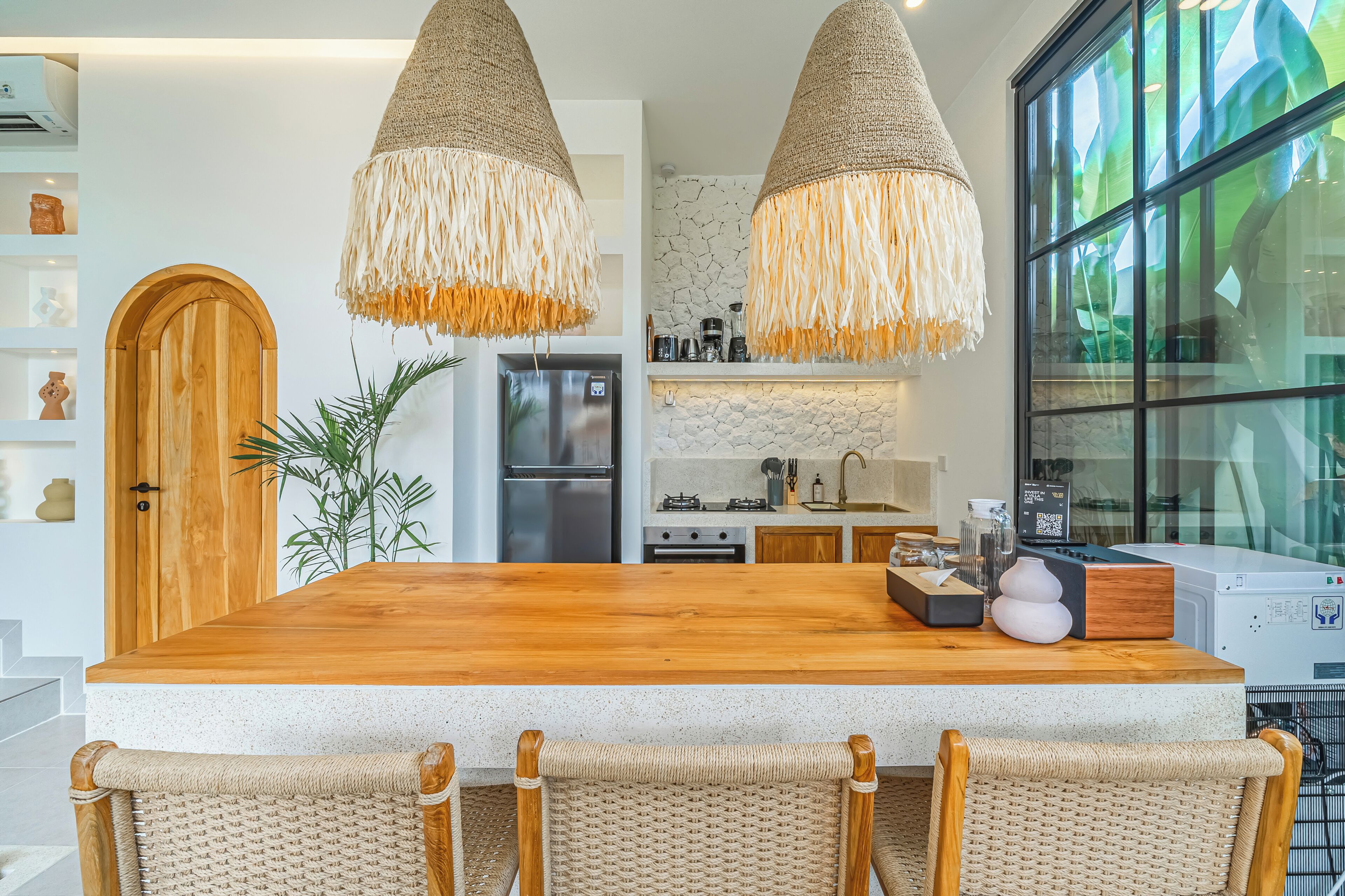 Een keuken met een houten kookeiland, geweven hanglampen en een betegelde achterwand.