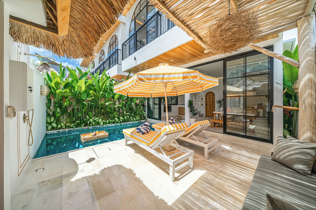 Un área de piscina interior moderna con sillones de descanso, una sombrilla grande y vistas a un muro verde y exuberante.
