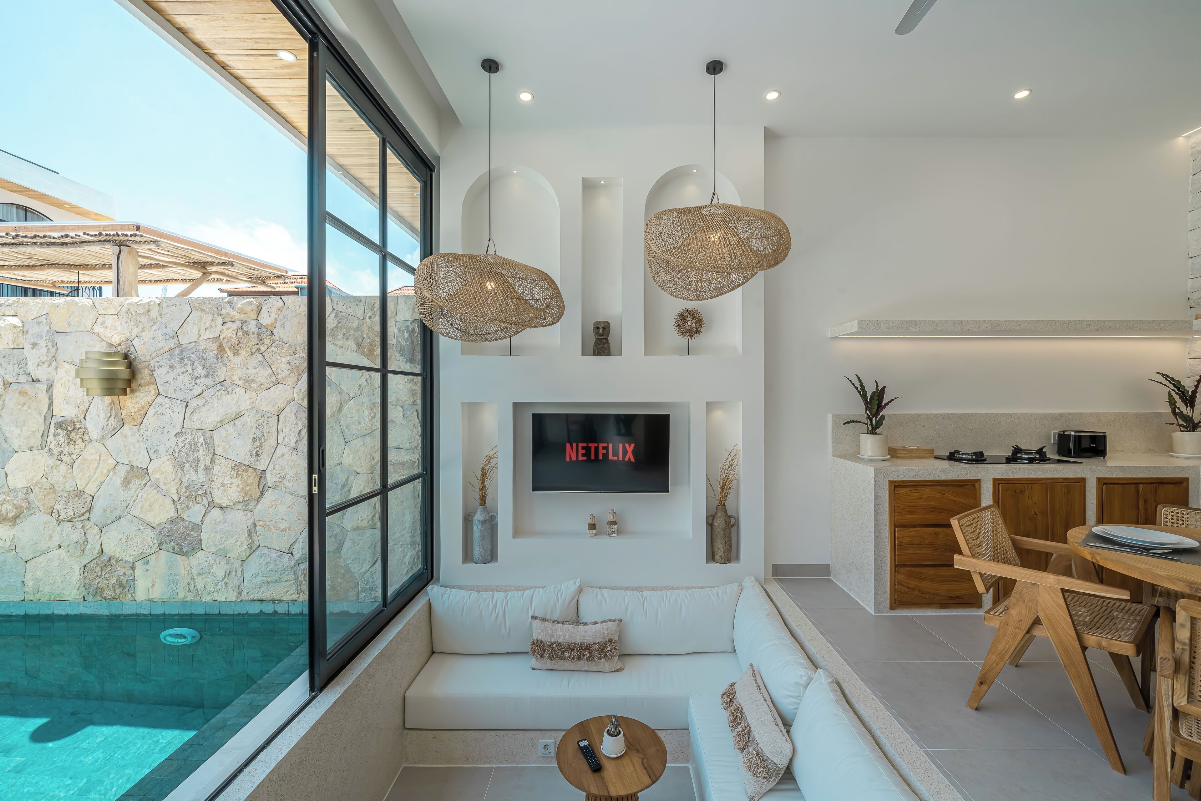 A modern living area with a stone wall, a pool, a sofa, a TV, and a dining area.
