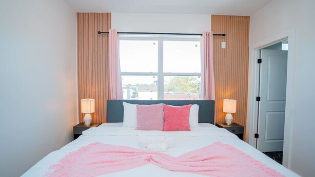 A hotel room with a bed, two bedside lamps, a window with curtains, and a view of the outside.