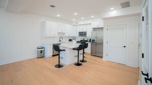 A modern kitchen with white cabinets, a central island with bar stools, stainless steel appliances, and a white door.