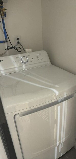 A white LG front-loading washing machine in a room with a plain wall and a visible electrical outlet.