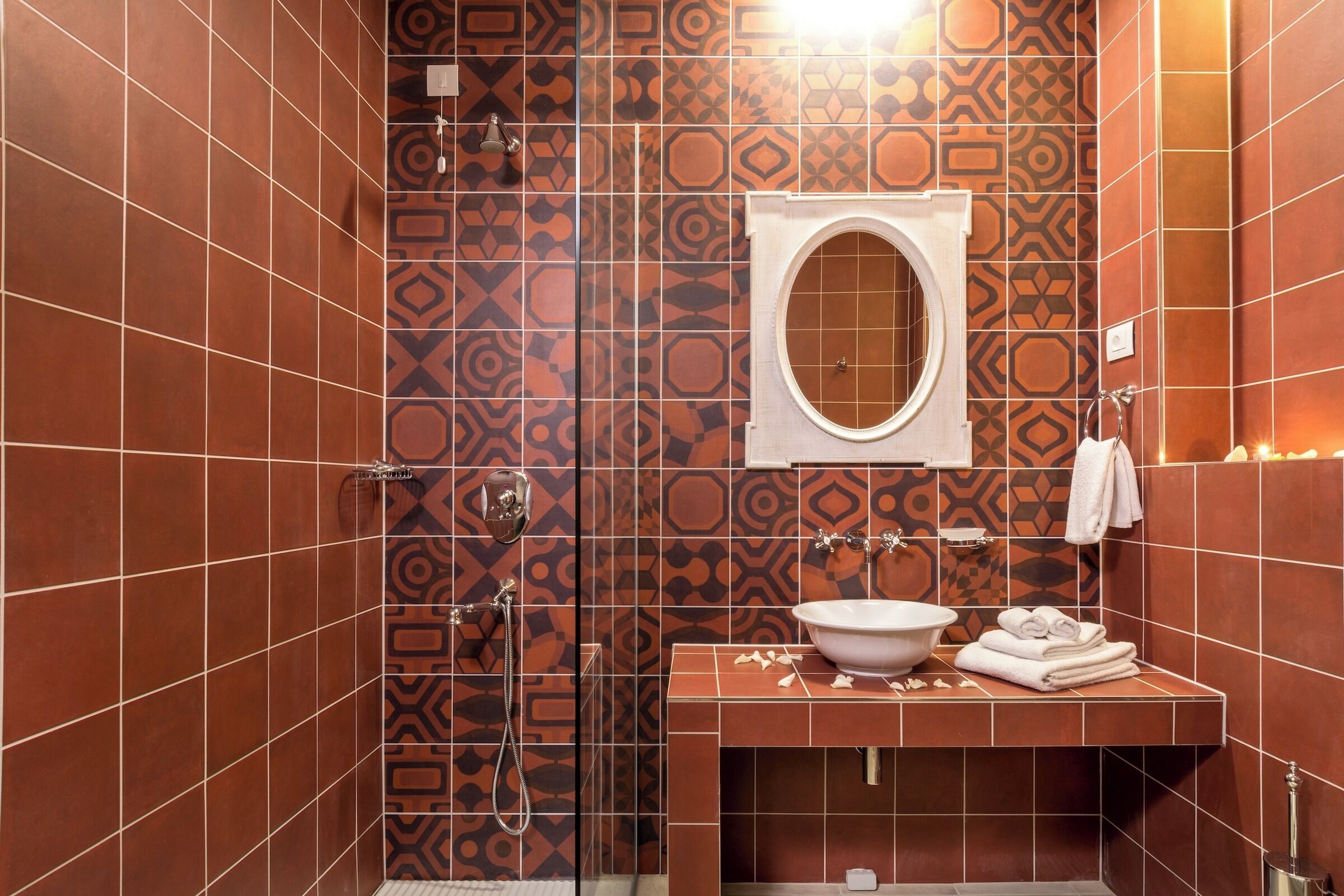 A bathroom with patterned tiles, a round mirror, a sink, and a shower.